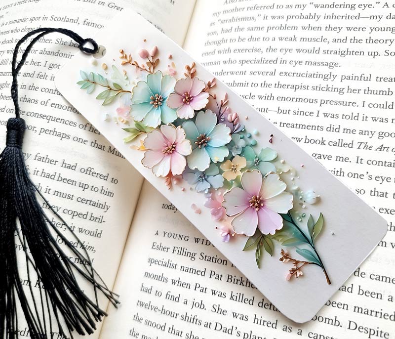 A collection of big and small flowers bookmark, in 3D style. The bookmark is a gift, and is sitting a a page of writing as the background. Very pretty bookmark, with a black tassel and made of aluminium.