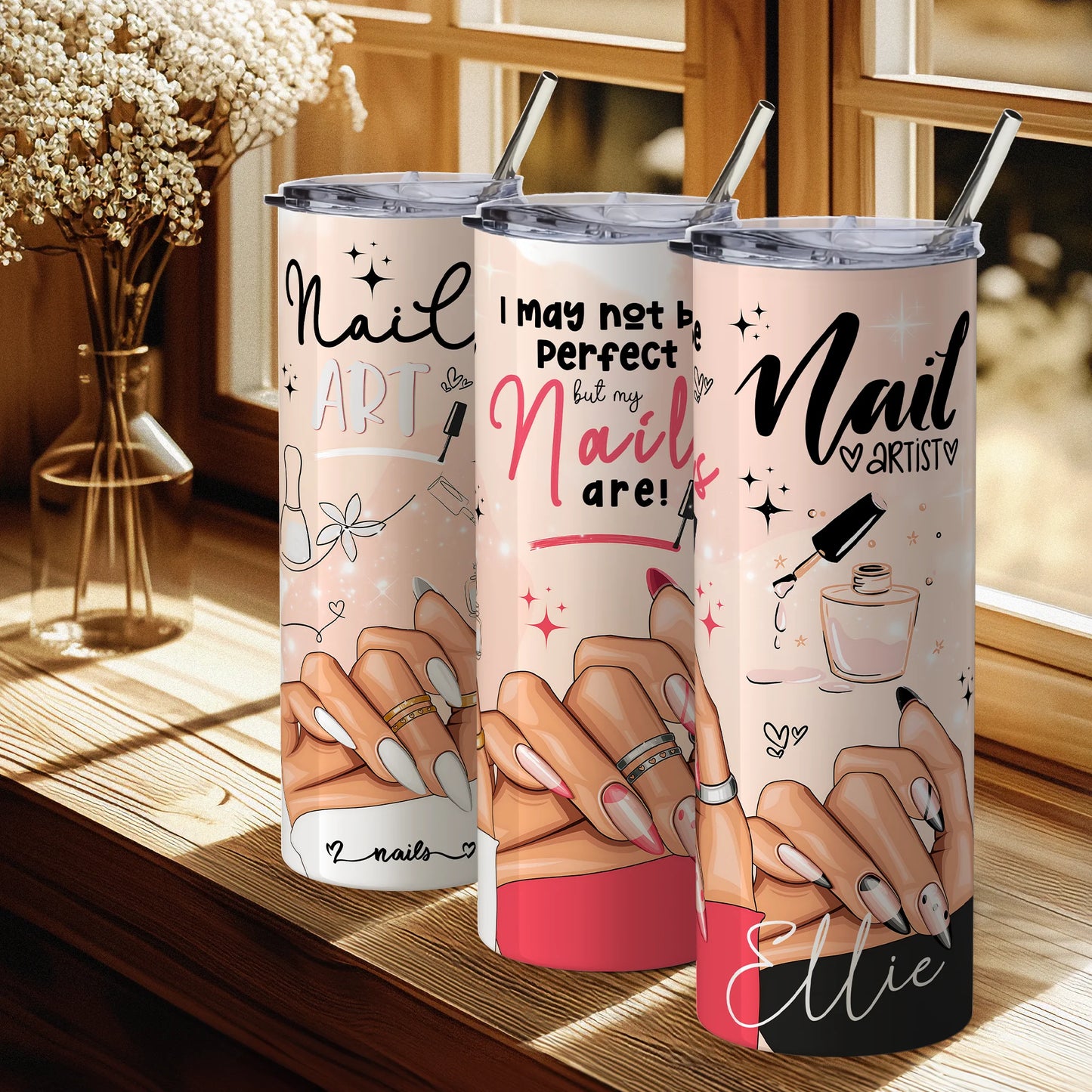 Three tumbler cups with nail art designs and text on a wooden surface.