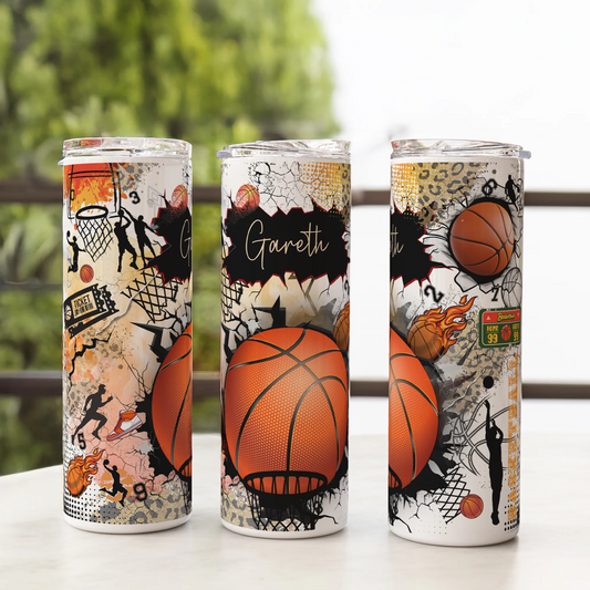 Three tumbler cups with basketball-themed designs on a surface with a blurred green background.