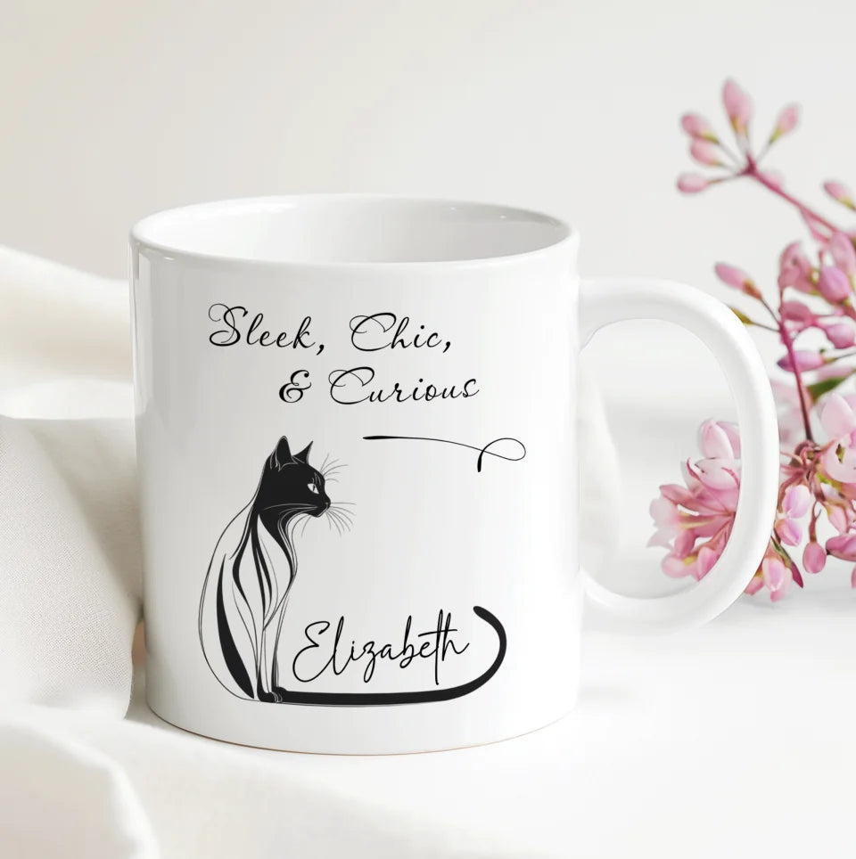 White mug with black cat illustration and text on a white background with pink flowers.