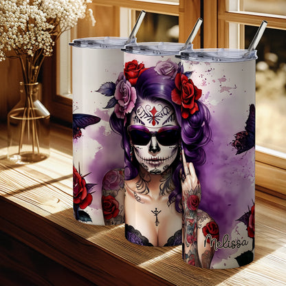 Tumbler with a colorful design of a woman with a skull makeup and tattoos, placed on a wooden surface.