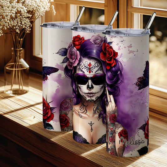 Tumbler with a colorful design of a woman with a skull makeup and tattoos, placed on a wooden surface.
