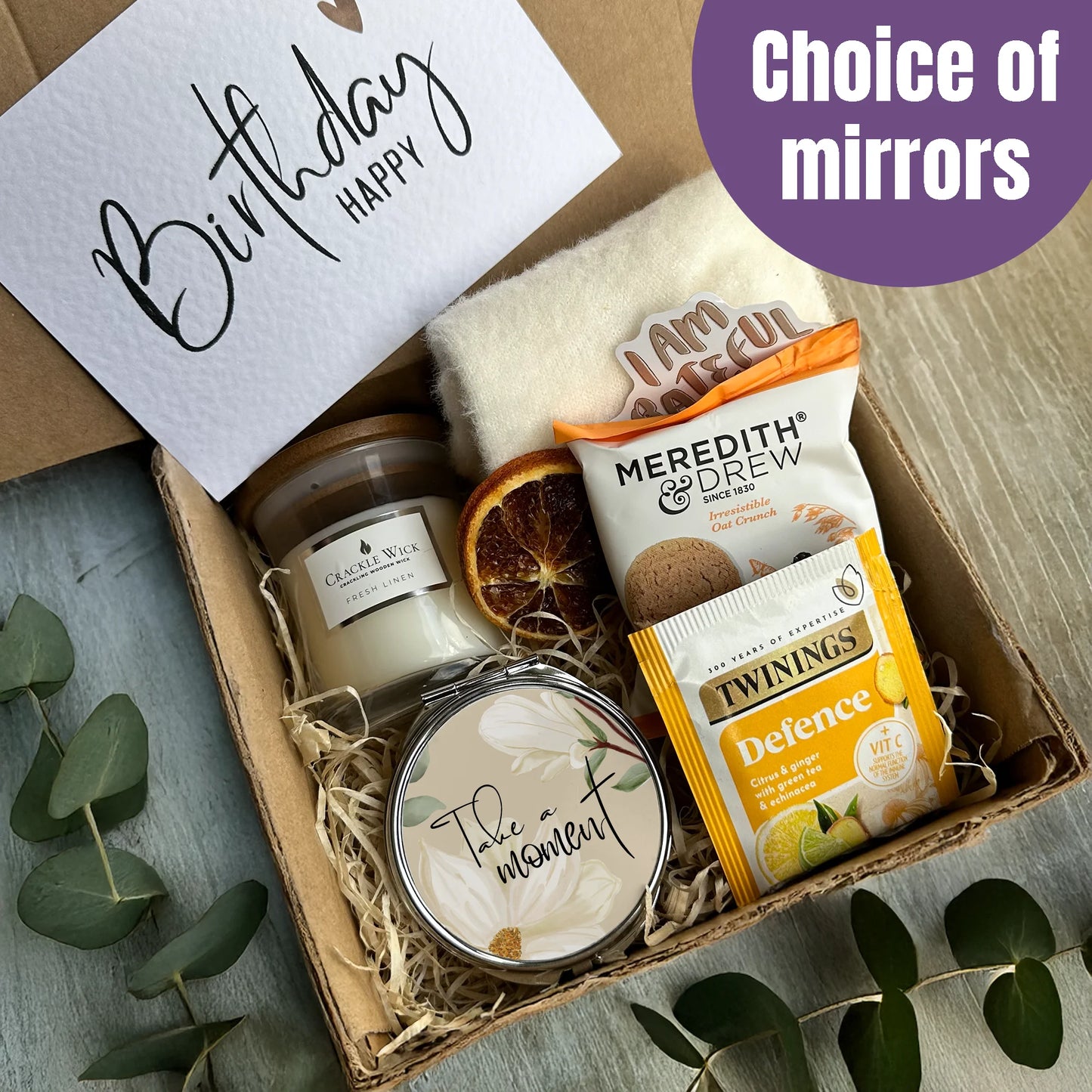 Gift box with candles, tea, and a card on a wooden surface