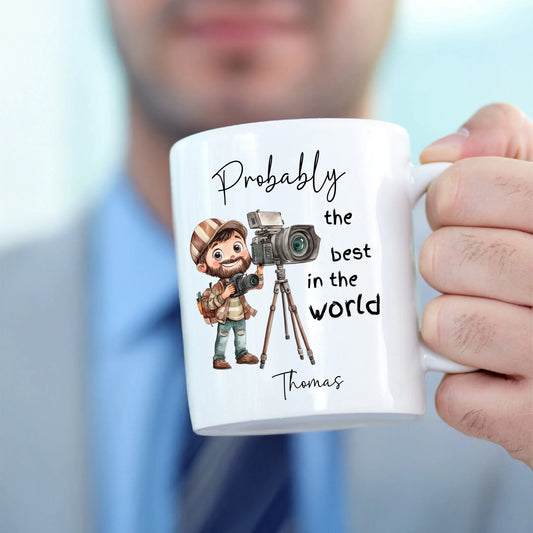 Mug with a cartoon character holding a camera and text 'Probably the best in the world' held by a person.
