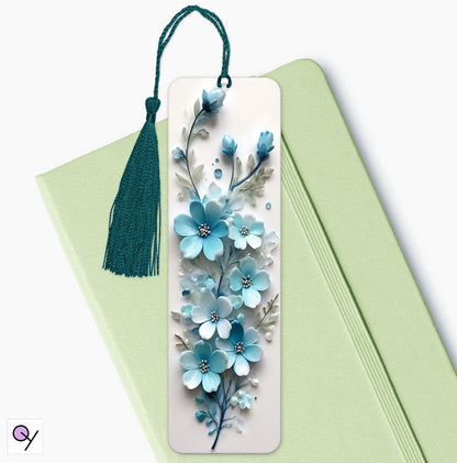 Aluminum bookmark featuring a striking 3D effect floral print of blue and white flowers, elegant and vibrant. The bookmark is sitting on a green diary.