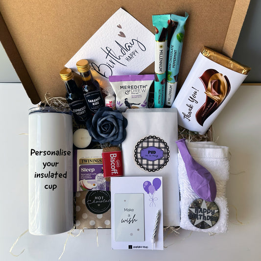 Gift basket with various items including a tumbler, snacks, and a card on a white surface.