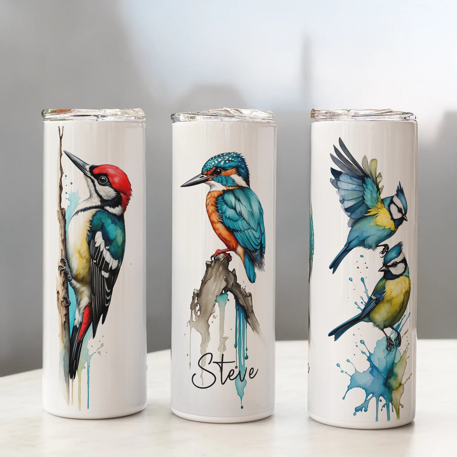 Three white tumblers with bird illustrations on a gray background