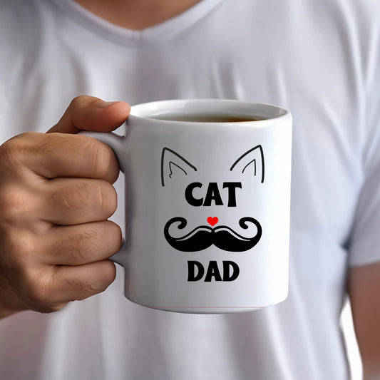 Person holding a white mug with 'Cat Dad' design on a plain background
