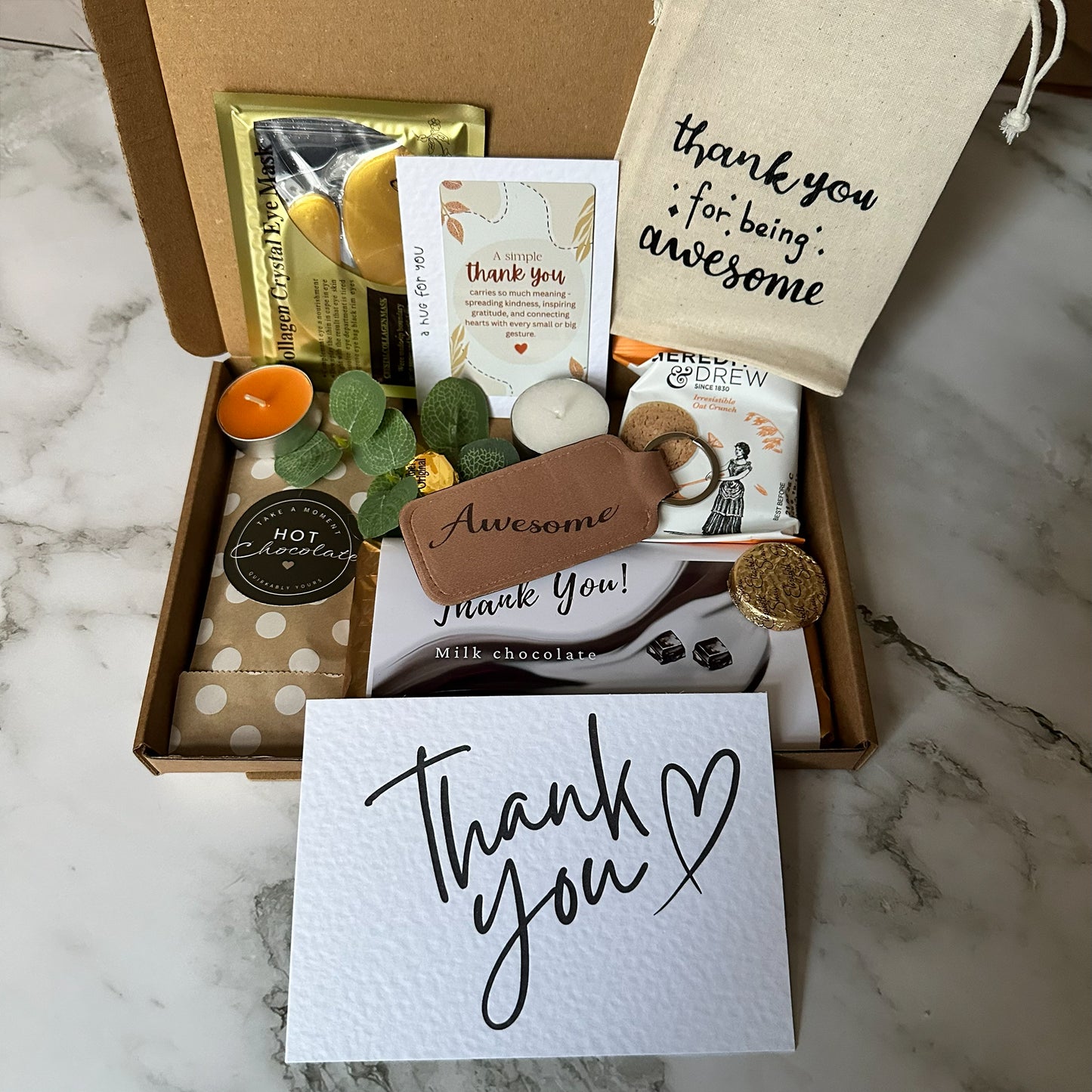 Gift box with 'thank you' card, candles, and other items on a marble surface - thank you letterbox gift with treat