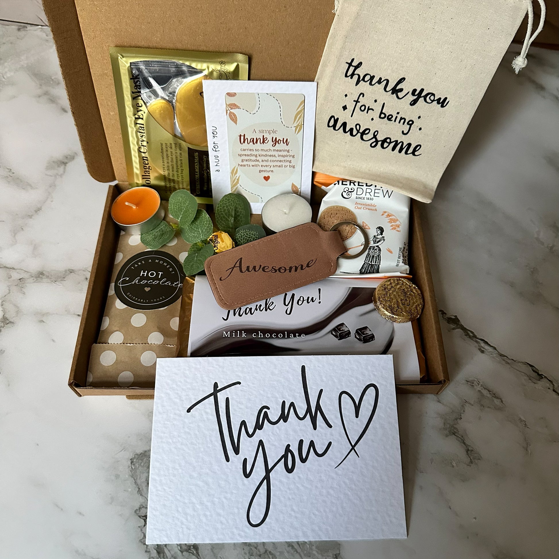 Gift box with 'thank you' card, candles, and other items on a marble surface - thank you letterbox gift with treat