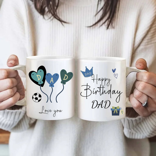Two mugs with birthday-themed designs for a father, held by a person wearing a light sweater.