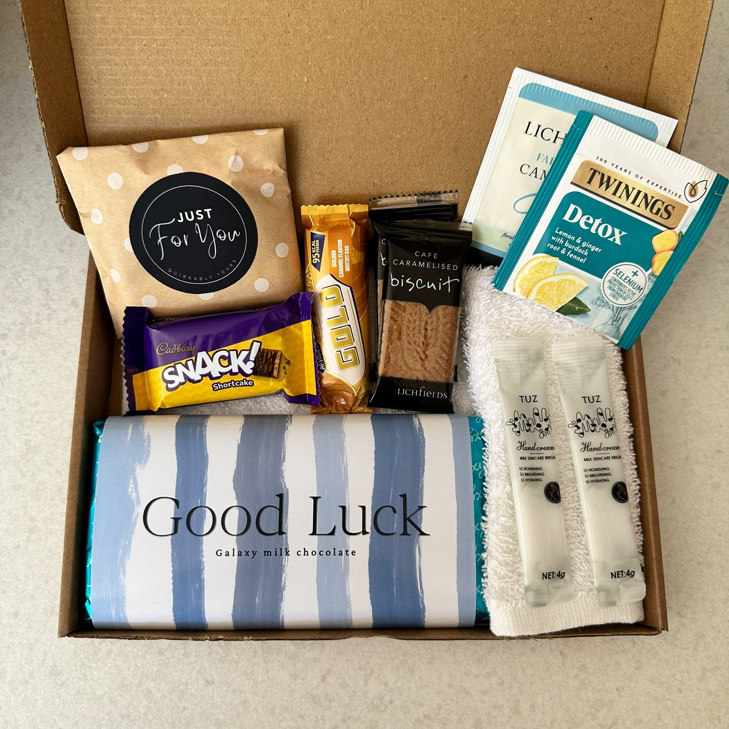 A good luck Gift box with various items including a chocolate bar, snacks, and tea packages.
