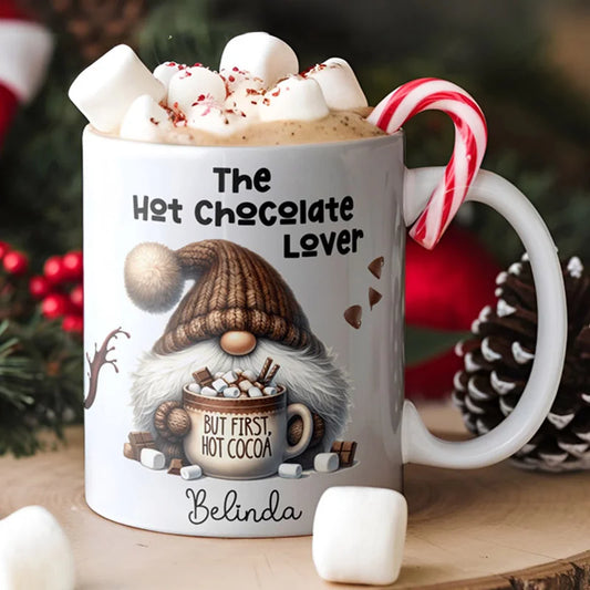 Mug with gnome design and 'The Hot Chocolate Lover' text, filled with hot chocolate and marshmallows, surrounded by Christmas decor.
