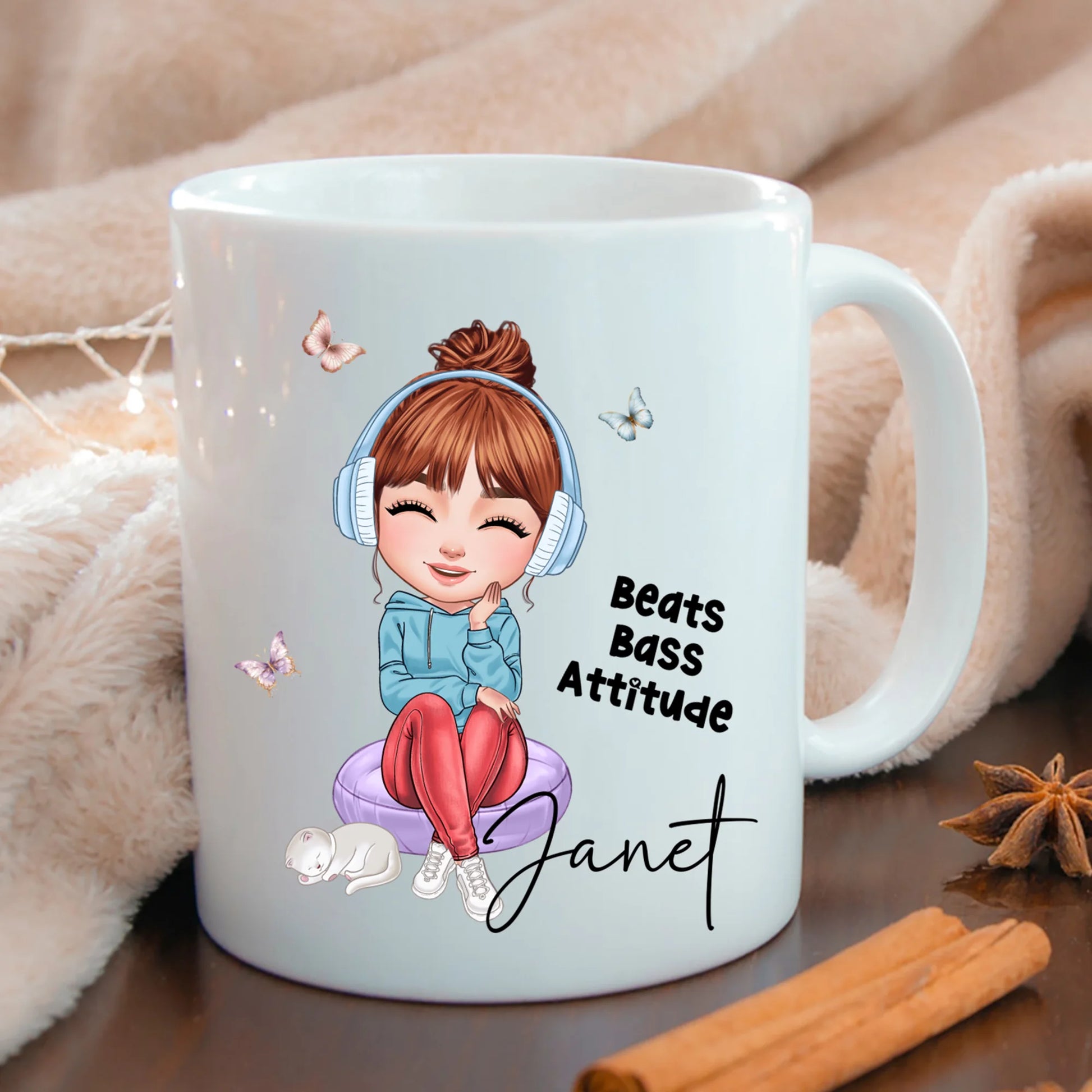 White mug with a cartoon character and text 'Beats Bass Attitude Janet' on a wooden surface.