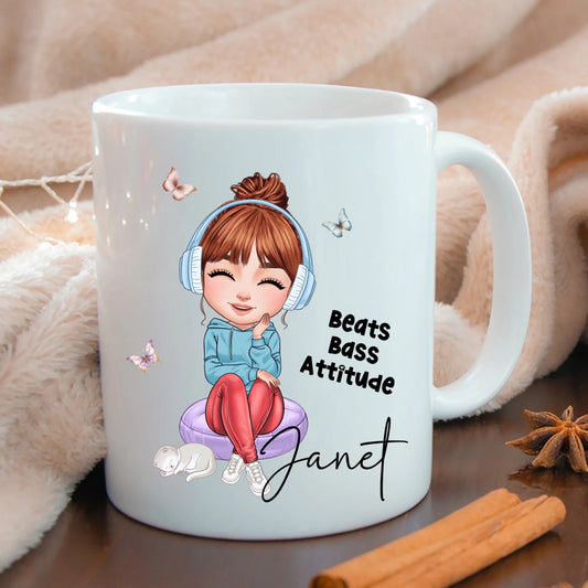 White mug with a cartoon character and text 'Beats Bass Attitude Janet' on a wooden surface.