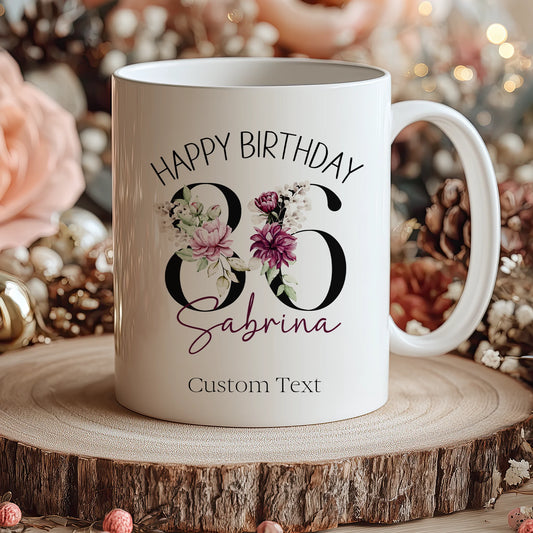 White mug with 'Happy Birthday Sabrina' text and floral design on a wooden surface with decorative background