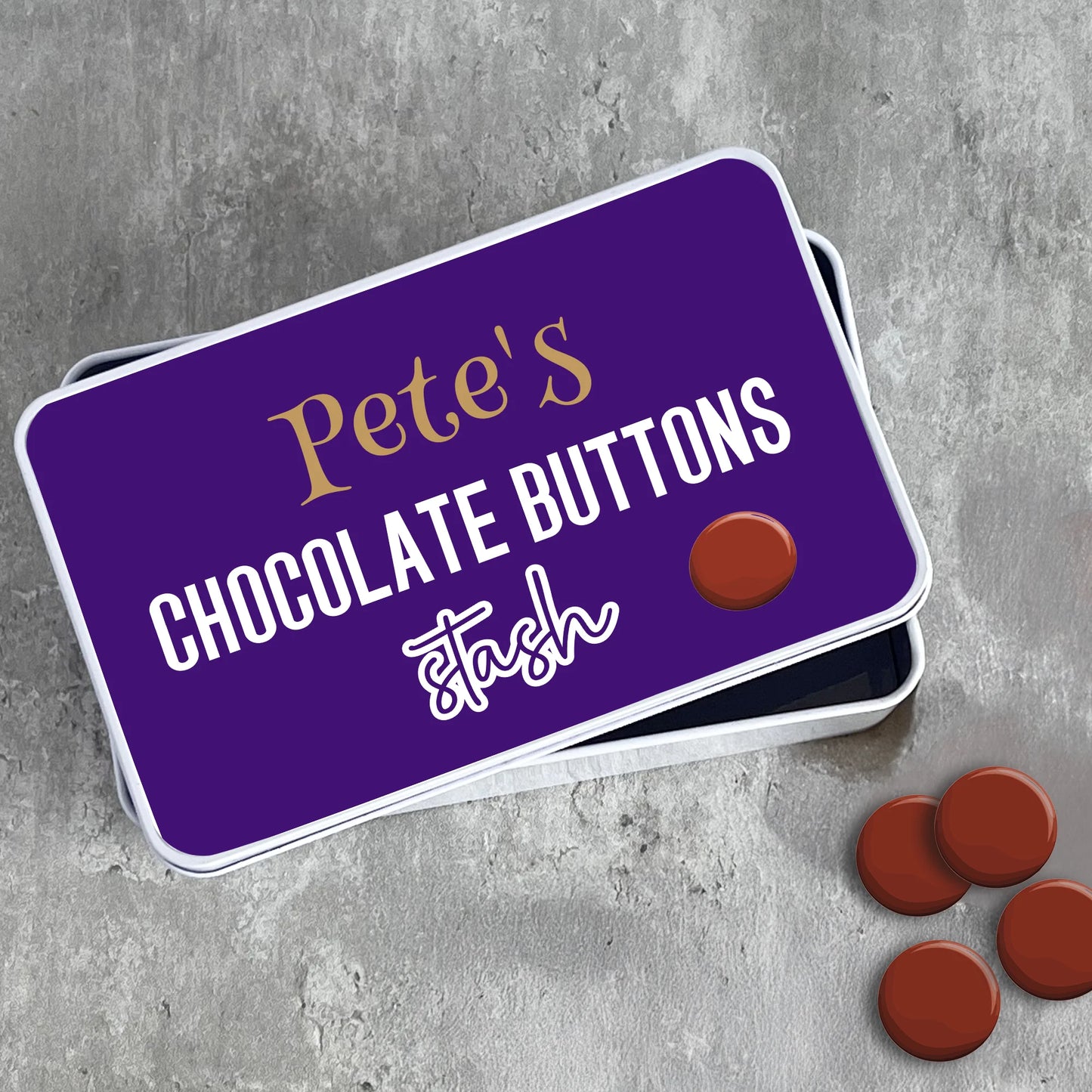 Purple tin labeled 'Pete's Chocolate Buttons stash' with chocolate buttons on a gray surface