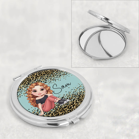 Compact mirror with a design of a woman on a leopard print background, on a white surface.