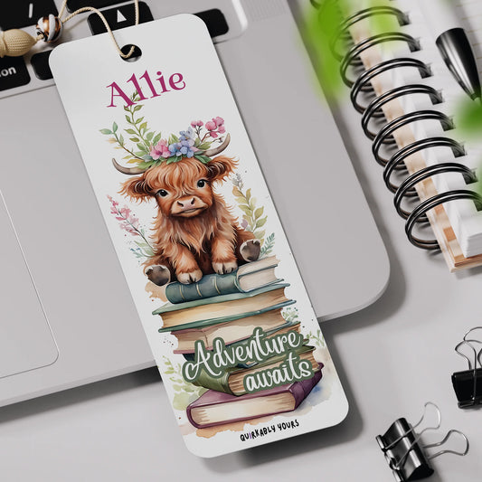 Bookmark with a cow illustration and 'Adventure awaits' text on a desk with stationery items.