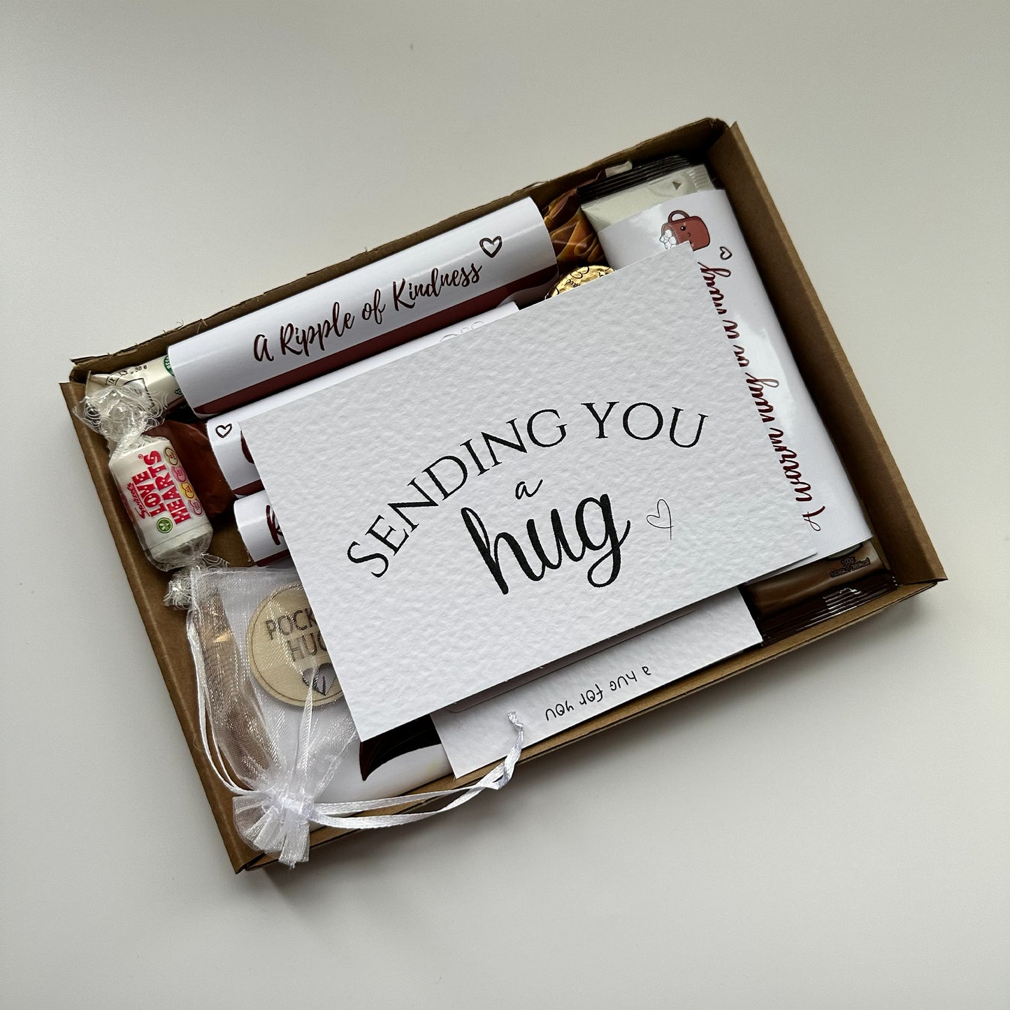 Letterbox-friendly Hug in a Box gift - Box of 'A Ripple of Kindness' with a card saying 'Sending You a Hug' on a light background