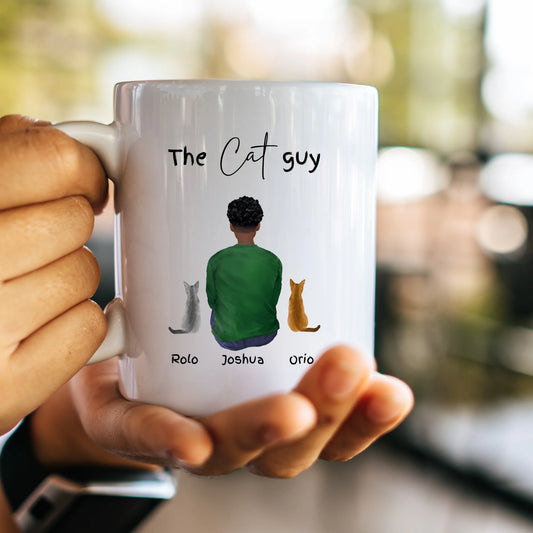 Person holding a mug with 'The Cat Guy' design featuring a person and three cats.